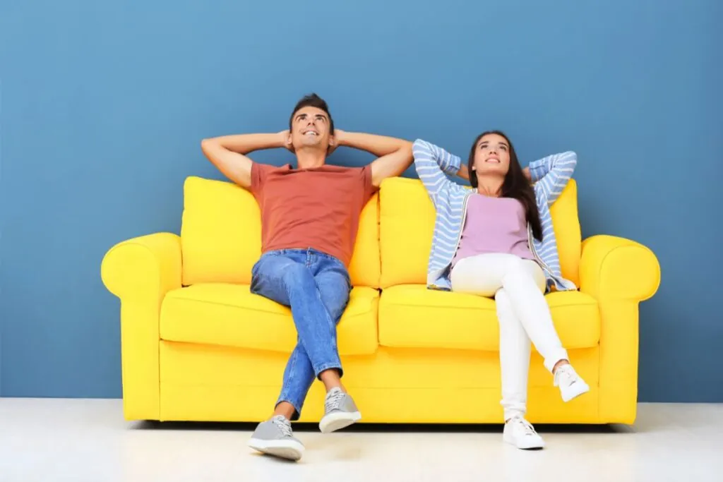 young couple relaxing on yellow sofa near color wall